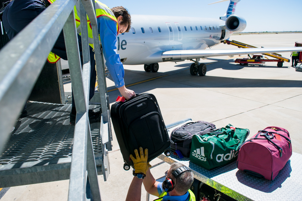 Lead Agent Skyler Reynolds reaches over the jet bridge to pick up valeted luggage. IMG_MAF_Skyler_Reynolds_AirportAgent-5