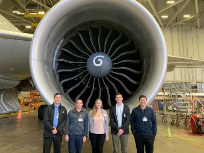 Five Envoy Cadet Instructors pose in the maintenance hangar in front of an aircraft